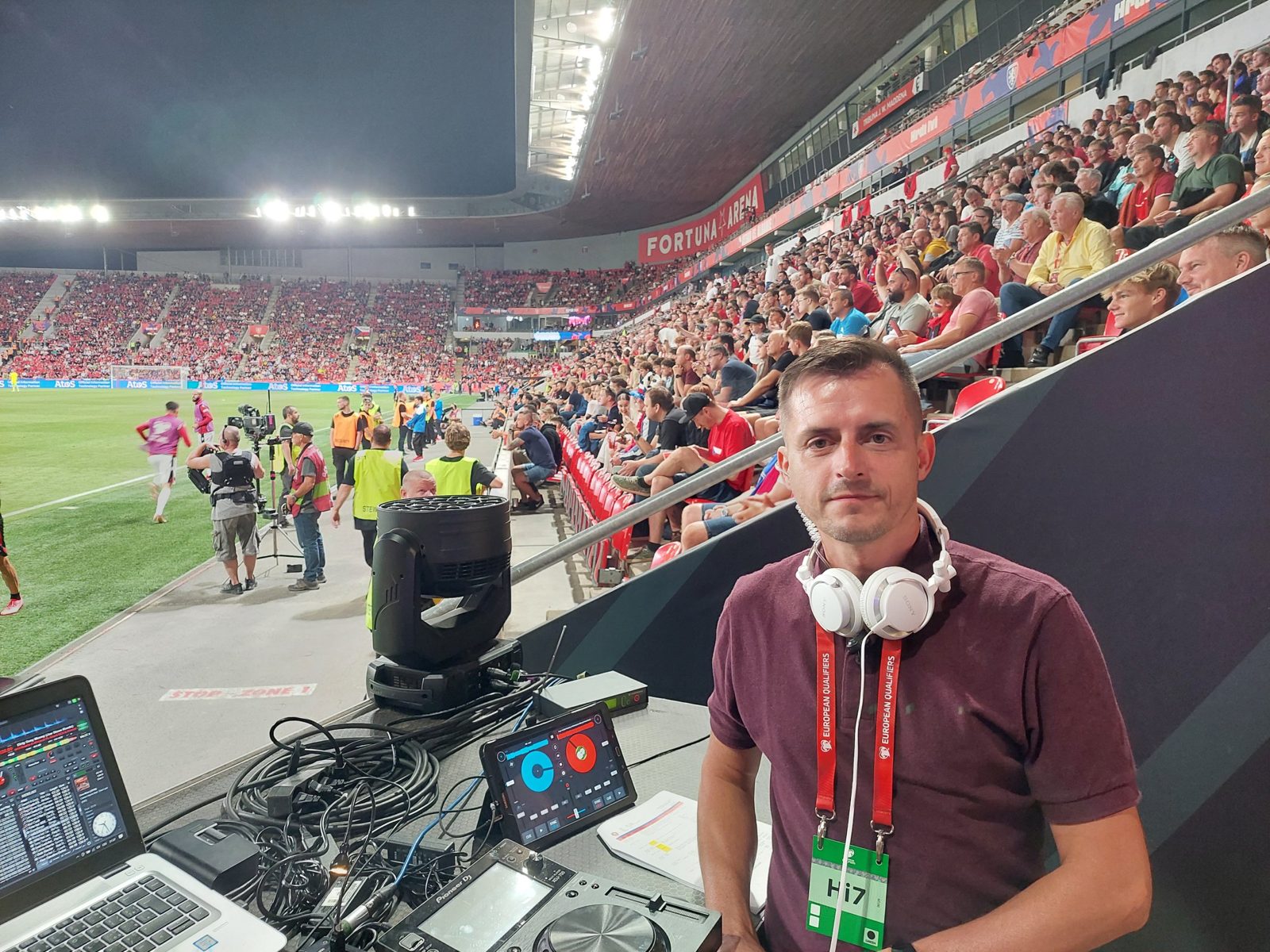 Jan Císař u DJ pultu na zápase reprezentace, za ním plná tribúna